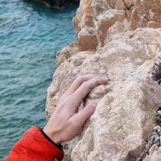 Kletterferien in Finale. Kletterhand umgreift Fels am Meer.
